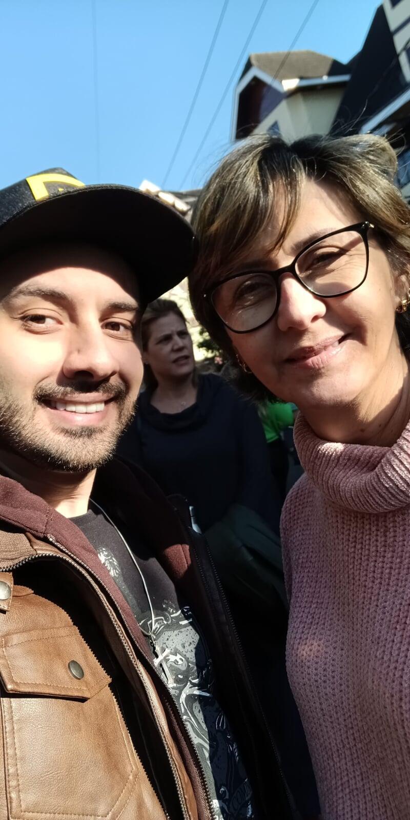 Imagem em formato de selfie de um jovem sorrindo com sua mãe.